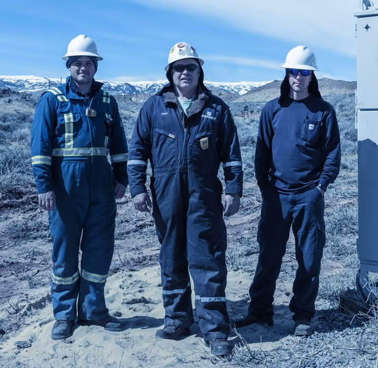 Three workers standing in front of distant snow-capped mountains on a VSD installation